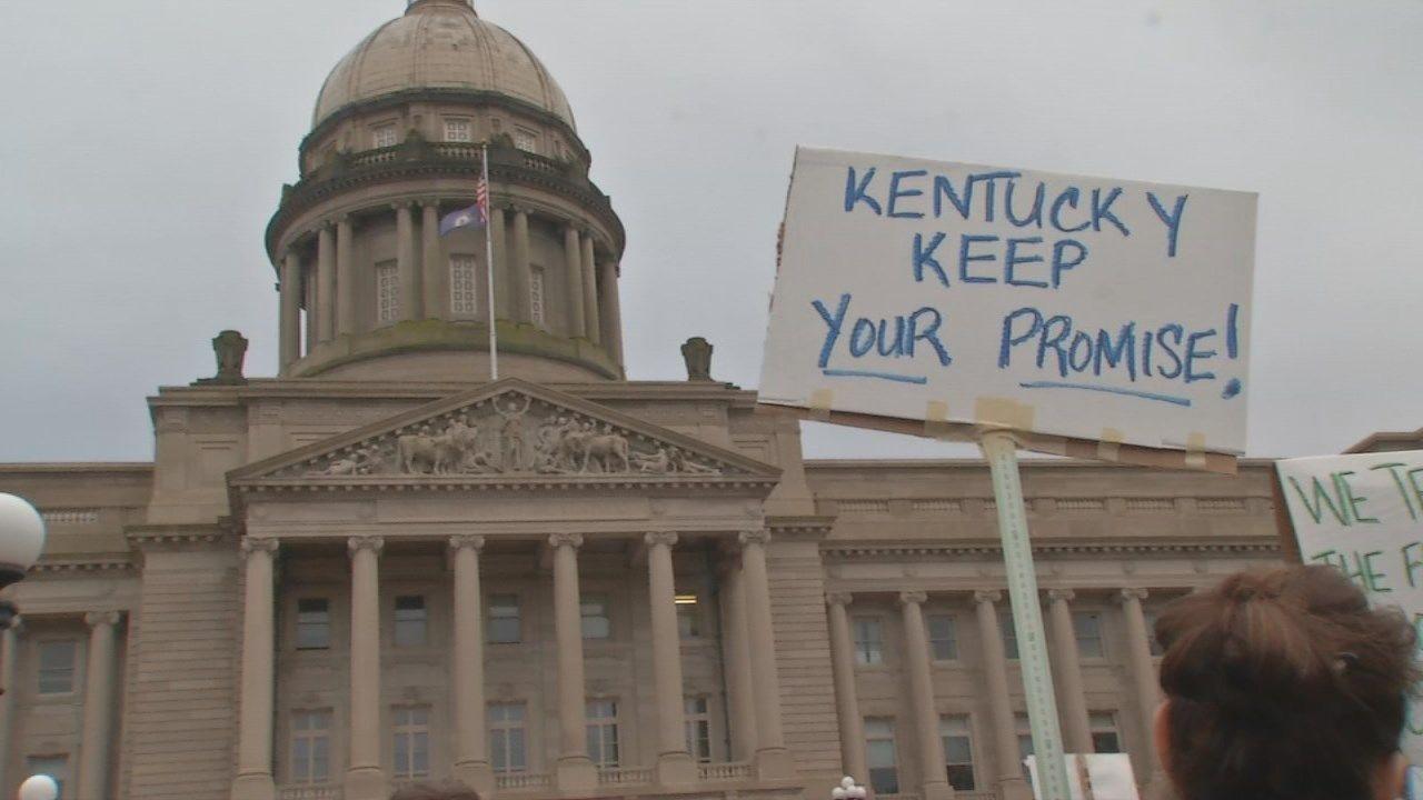 Distance shot of Frankfort capitol building with handmade sign from protestors raised in front that reads "Kentucky KEEP Your Promise"